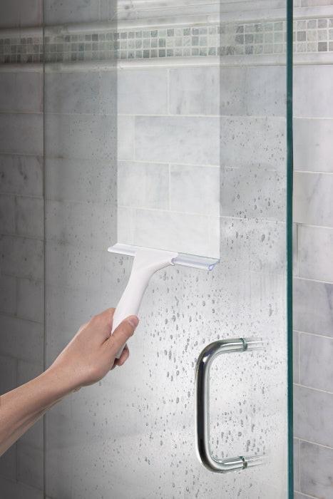 Hand mit Abzieher reinigt nasse Glasdusche im Badezimmer