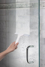 Hand mit Abzieher reinigt nasse Glasdusche im Badezimmer