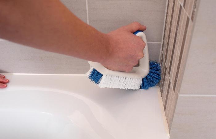 Hand reinigt Badewannenecke mit der robusten Unger Flachbürste mit blau-weißen Borsten