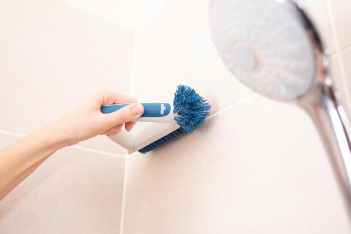 Hand hält Unger Eckreinigungsbürste zum Reinigen der Fliesenfugen in der Dusche