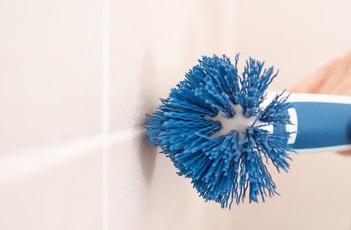 Nahaufnahme einer Hand mit Unger Eckreinigungsbürste beim Reinigen von Fliesenfugen