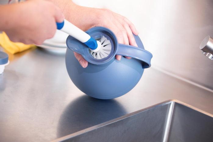 Hand hält Unger Spülbürste Flex mit blauem Griff beim Reinigen einer runden Kunststoffkanne in der Küche