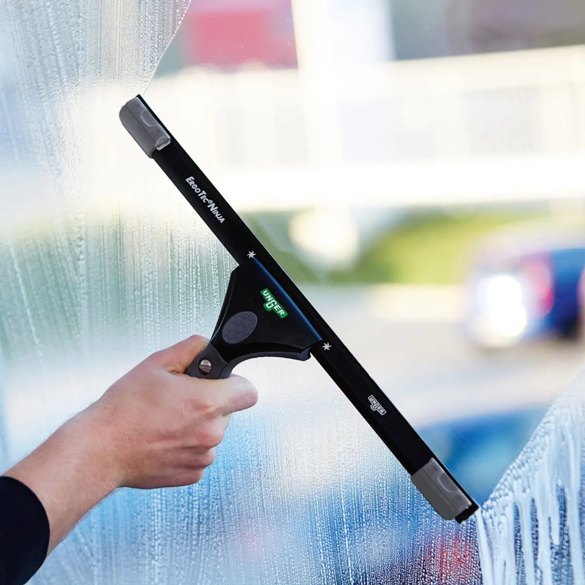 Hand mit UNGER ErgoTec Ninja Abzieher beim streifenfreien Reinigen einer Fensterscheibe