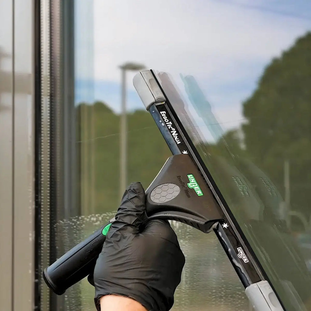 Hand mit schwarzem Handschuh hält UNGER ErgoTec Ninja Fensterwischer 40° vor Glasfassade