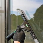 Hand mit schwarzem Handschuh hält UNGER ErgoTec Ninja Fensterwischer 40° vor Glasfassade