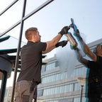 Mann reinigt mit dem UNGER ErgoTec Ninja 6in1 Fensterreinigungs-Set AKN14 eine große Glasfassade bei Tageslicht
