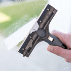 Hand hält Unger ErgoTec Ninja Schaber und entfernt Aufkleber von einer Glasoberfläche