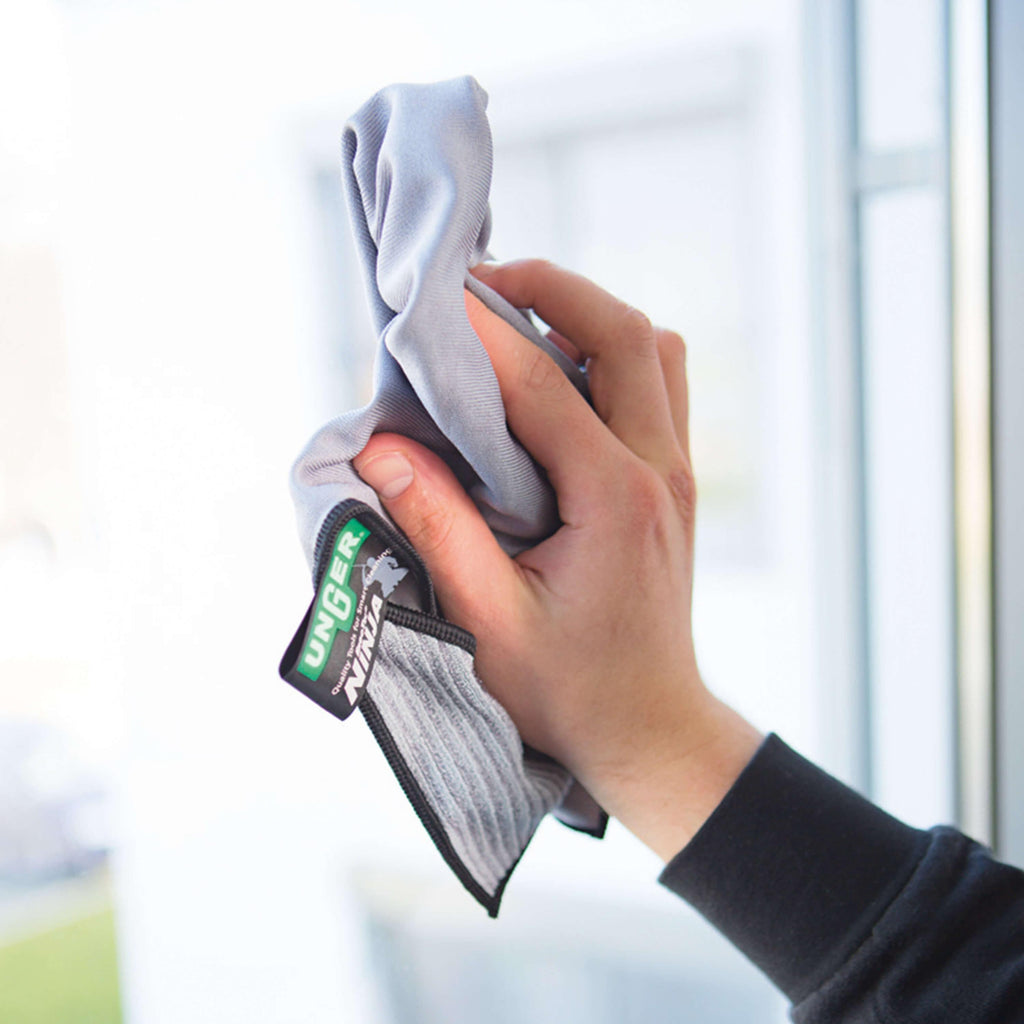 Hand wischt mit einem UNGER Mikrofasertuch der ErgoTec Ninja Serie über eine Fensterscheibe – Bestandteil des 6in1 Complete Kits AKN14