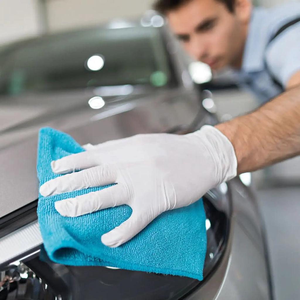 Hygostar safe premium weiße nitril handschuhe beim reinigen einer glänzenden schwarzen autofläche mit blauem microfiber tuch