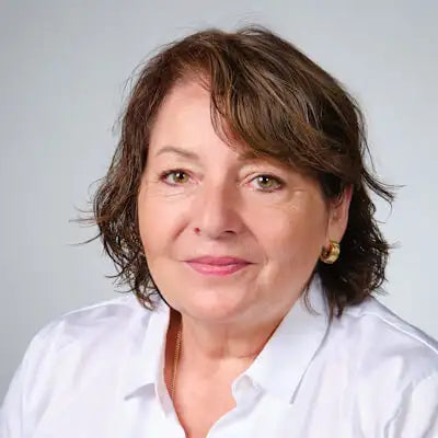 Porträt einer lächelnden Frau mit braunen Haaren und weißem Hemd vor hellem Hintergrund.