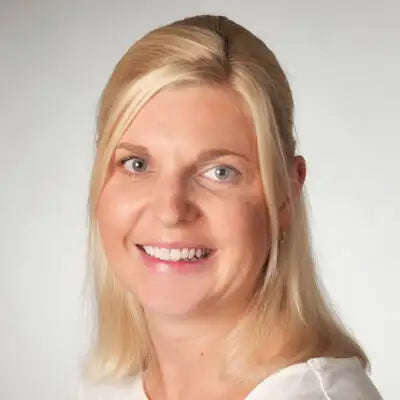 Porträt einer lächelnden Frau mit blonden Haaren vor neutralem Hintergrund