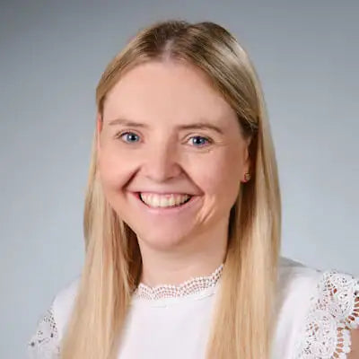 Porträt einer lächelnden Frau mit langen blonden Haaren vor neutralem Hintergrund, freundlich und einladend.