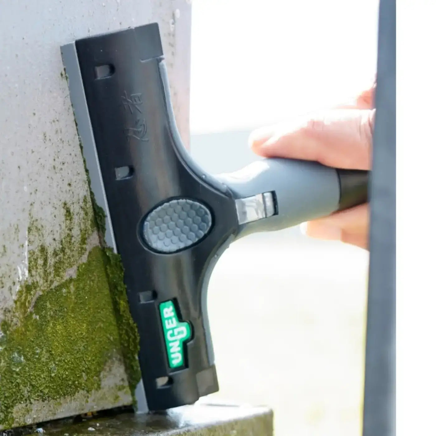 Black and gray unger Kunststoffklingen squeegee with textured grip handle used to remove green moss from surface