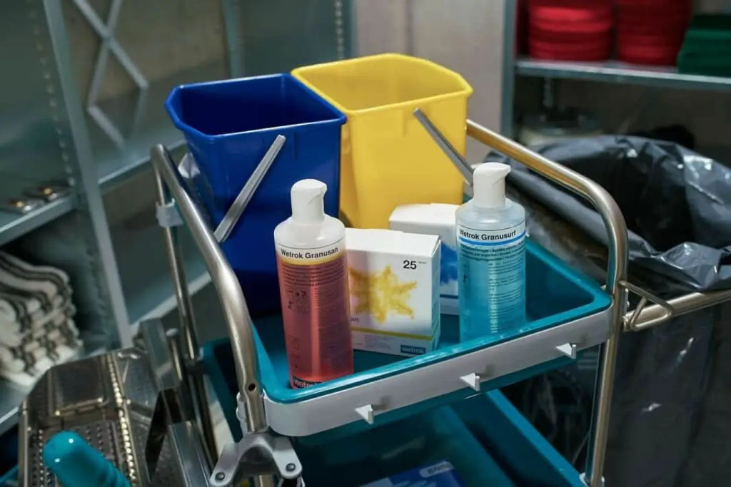 Blaue und gelbe plastik eimer mit metallgriffen auf einem medizinwagen neben flaschen mit wetrok granuusan desinfektionsmittel
